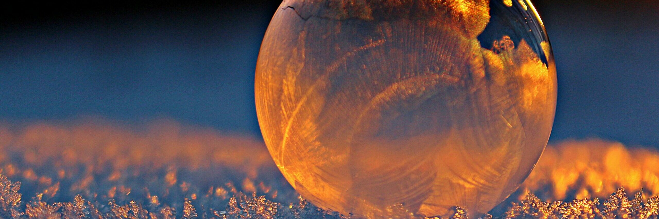 Close-up shot of a frozen bubble with warm reflections resting on a snowy surface at twilight.